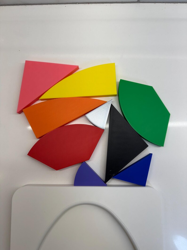 Op de afbeelding: Een set kleurrijke geometrische vormen, waaronder een roze driehoek, een gele halve maan, een oranje halve maan, een rode halve maan, een groene halve maan, een zwarte driehoek, een zilveren driehoek, een blauwe driehoek en een paarse halve maan.