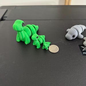 Puede incluir: Tres figuras de dinosaurio impresas en 3D de diferentes tama&ntilde;os, la m&aacute;s grande es aproximadamente del tama&ntilde;o de una moneda de 20 c&eacute;ntimos de euro. Los dinosaurios tienen ojos grandes y est&aacute;n segmentados.