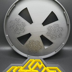 May include: A gray plastic circular puzzle with three interlocking geometric shapes. The puzzle is designed to be disassembled and reassembled. The puzzle is shown on a black surface.