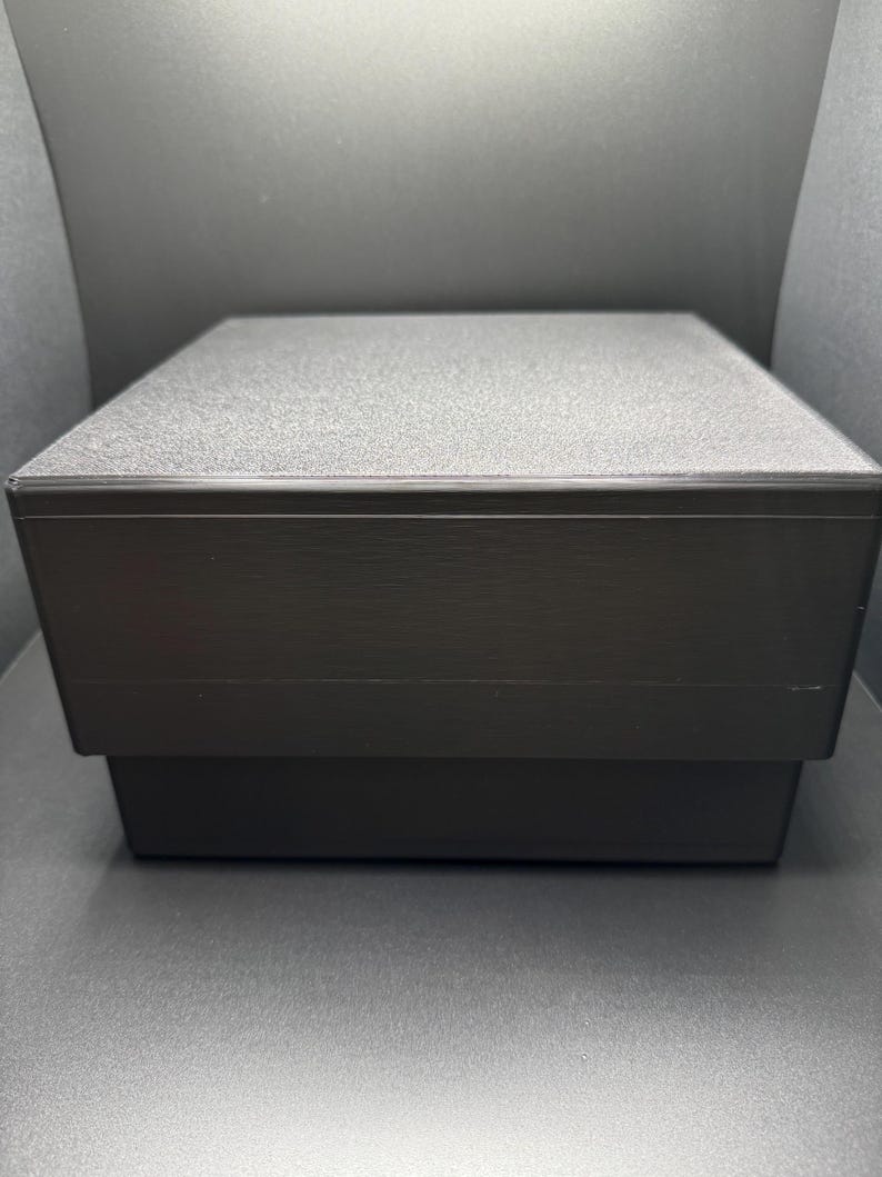 May include: A black square box with a textured lid. The box is closed.
