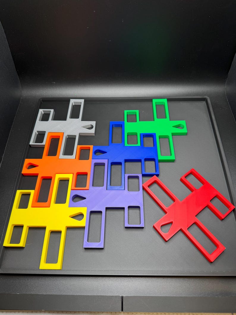 K&ouml;nnte beinhalten: Eine Sammlung farbenfroher, geometrischer Puzzleteile in verschiedenen Formen und Gr&ouml;&szlig;en. Die Teile sind in Rot-, Orange-, Gelb-, Gr&uuml;n-, Blau-, Lila- und Graut&ouml;nen gehalten. Die Puzzleteile sind auf einer dunklen Oberfl&auml;che angeordnet.