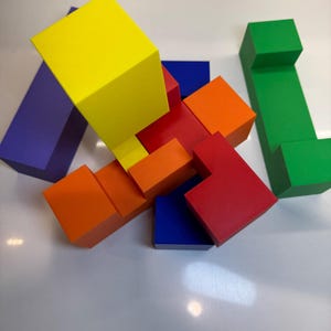 May include: A colorful wooden puzzle with blocks in red, orange, yellow, blue, green, and purple. The blocks are arranged in a complex pattern, creating a challenging puzzle.