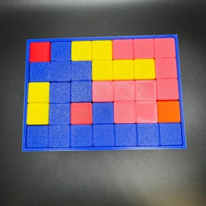 May include: A colorful puzzle game with a blue frame. The puzzle pieces are various colors, including red, yellow, pink, and orange. The game is designed with a grid of squares, and the pieces fit into the grid.