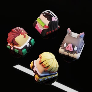 May include: Four colorful keycaps featuring characters from the anime Demon Slayer. The keycaps are made of plastic and have a 3D design. The keycaps are in the colors of pink, green, yellow, and brown.