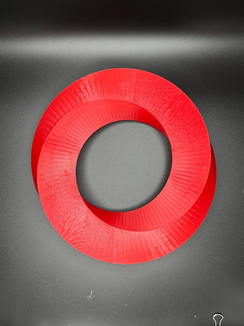 May include: A red, 3D printed, Mobius strip shaped ring. The ring is made of plastic and has a smooth, glossy finish.