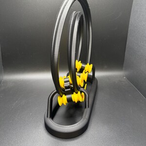 May include: A black and yellow kinetic sculpture with a looping design. The sculpture features three black circular tracks with yellow accents and a black base. The design is modern and geometric.