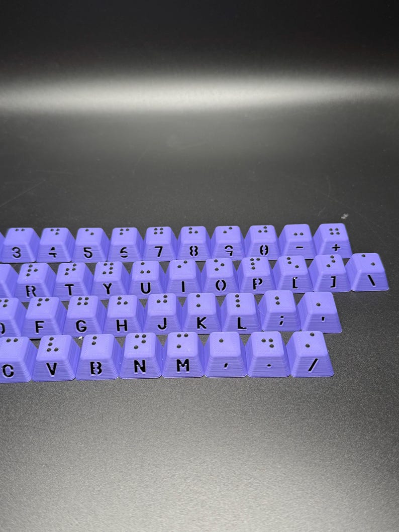 May include: A set of purple keyboard keys with black lettering and braille dots. The keys include numbers, letters, punctuation marks, and symbols.