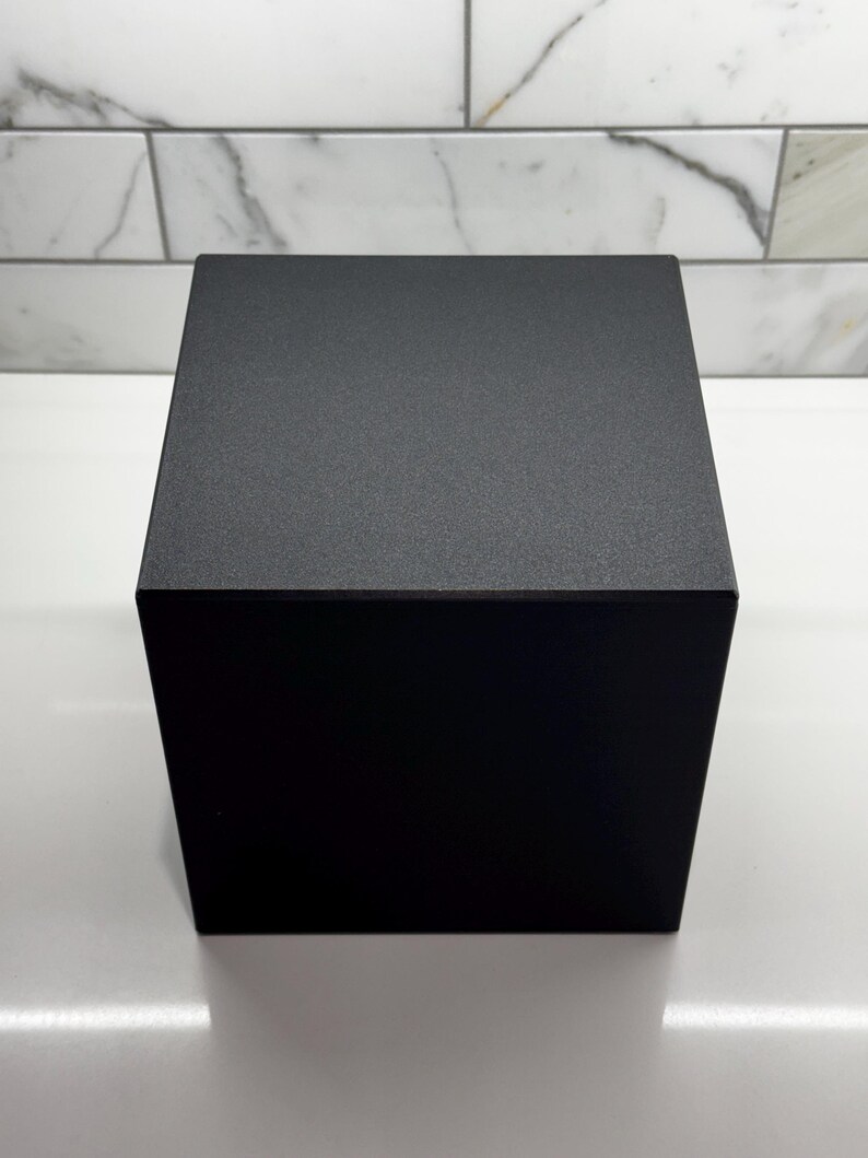 May include: A black cube-shaped box with a textured surface.