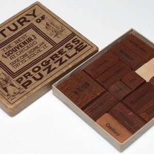 May include: A wooden box with a brown paper label that reads "Century of Progress Puzzle" and "The Best Souvenir at Chicago. Take one home and try to solve it." The box contains a wooden puzzle with 12 pieces, each with a different word printed on it.
