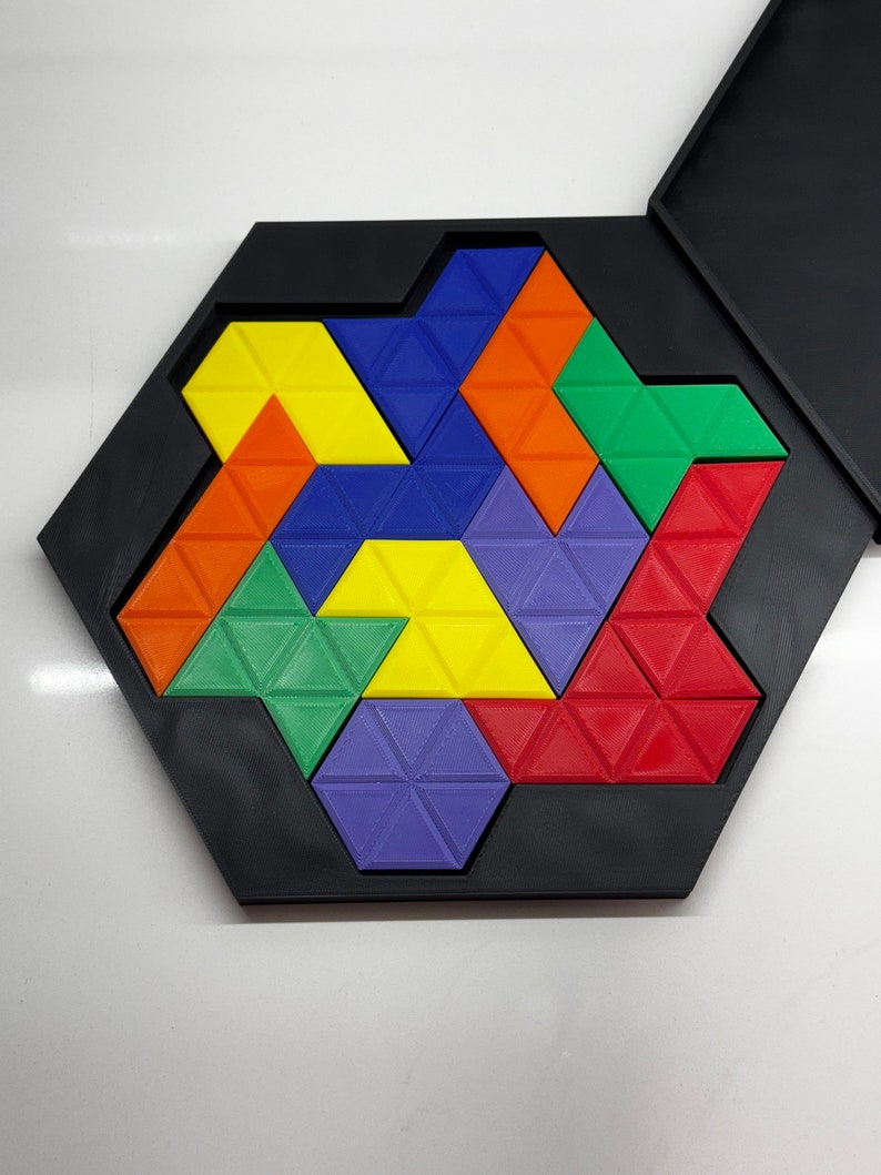 Op de afbeelding: Een zeshoekige puzzel met een zwart frame en een kleurrijk geometrisch ontwerp. De puzzel is gemaakt van driehoekige stukken in rood, oranje, geel, groen en paars.