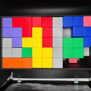 Op de afbeelding: Een kleurrijke puzzel met een verscheidenheid aan gekleurde vierkanten die in een patroon zijn gerangschikt. De puzzel bestaat uit rode, blauwe, groene, gele, oranje, paarse en grijze vierkanten.
