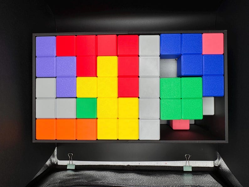 Op de afbeelding: Een kleurrijke puzzel met een verscheidenheid aan gekleurde vierkanten die in een patroon zijn gerangschikt. De puzzel bestaat uit rode, blauwe, groene, gele, oranje, paarse en grijze vierkanten.