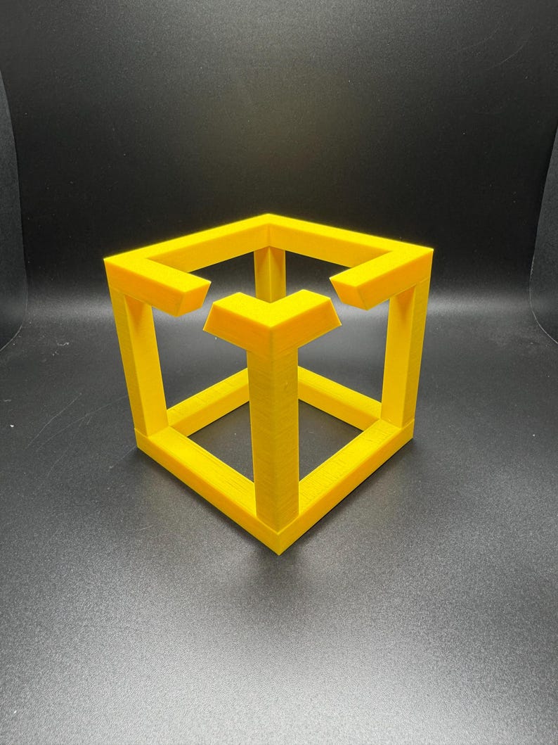 May include: A yellow impossible cube sculpture, a 3D-printed optical illusion. The cube appears to defy the laws of physics with its interconnected, yet seemingly impossible, structure. The sculpture is a bright, solid yellow color.