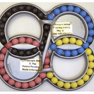 May include: A silver-colored puzzle toy with an infinity symbol design. The toy features colored balls in black, pink, blue, and yellow. The text on the toy reads "Copyright 1982 E. Pap Patent Pending Made in Hungary."