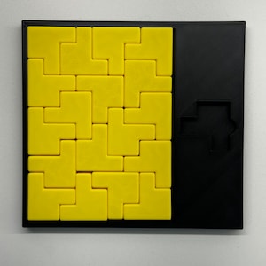 May include: A yellow puzzle with a black frame. The puzzle is made up of small, square pieces that fit together to form a larger shape. The puzzle is missing one piece, which is shown in the black frame on the right side of the image.