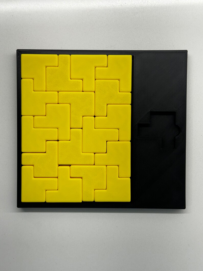 May include: A yellow puzzle with a black frame. The puzzle is made up of small, square pieces that fit together to form a larger shape. The puzzle is missing one piece, which is shown in the black frame on the right side of the image.