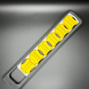 May include: A black and white plastic tool with a handle and a row of yellow, circular cutouts.