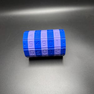 May include: A blue and purple combination lock with numbers. The cylindrical lock has a series of numbers and squares in blue and purple. The numbers are white. The lock is on a black surface.