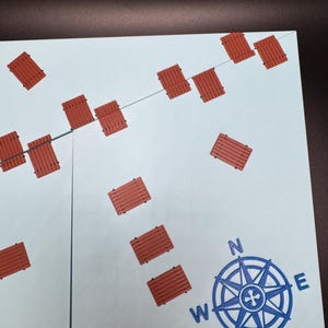 May include: A light blue map with a compass rose and several small, rectangular, reddish-brown objects. The compass rose is blue and indicates the cardinal directions. The objects are arranged in a scattered pattern.