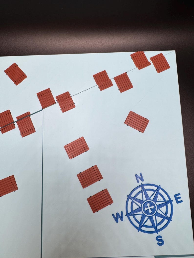 May include: A light blue map with a compass rose and several small, rectangular, reddish-brown objects. The compass rose is blue and indicates the cardinal directions. The objects are arranged in a scattered pattern.