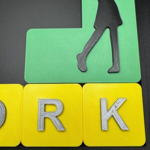 May include: A green and yellow 3D word art piece that spells out the word "WORK" with a silhouette of a person playing golf on top.