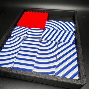 May include: A set of blue and white striped tiles with a red tile in the centre. The tiles are arranged in a wave pattern and are in a black tray.