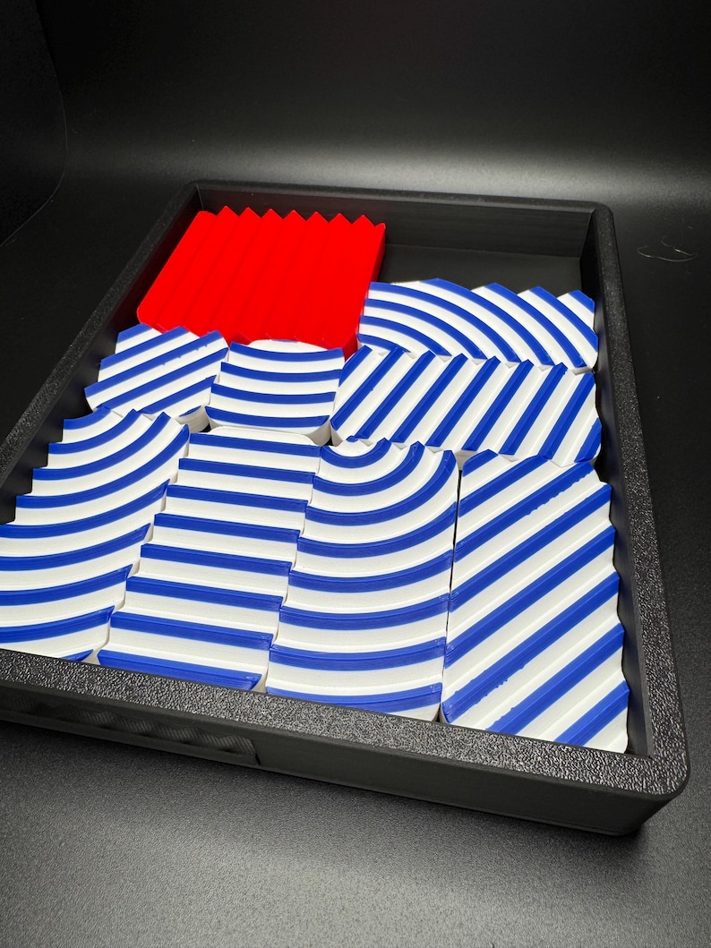 May include: A set of blue and white striped tiles with a red tile in the centre. The tiles are arranged in a wave pattern and are in a black tray.