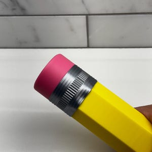 May include: A yellow pencil-shaped water bottle with a pink eraser top and a silver band.