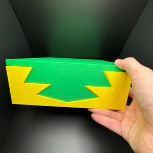 May include: A green and yellow interlocking puzzle made of three pieces. The puzzle is made of a hard plastic material.