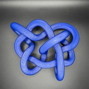 K&ouml;nnte beinhalten: Eine blaue, 3D-gedruckte Knotenskulptur. Der Knoten besteht aus einem einzigen St&uuml;ck Plastik und ist in einem komplexen Muster gebunden.