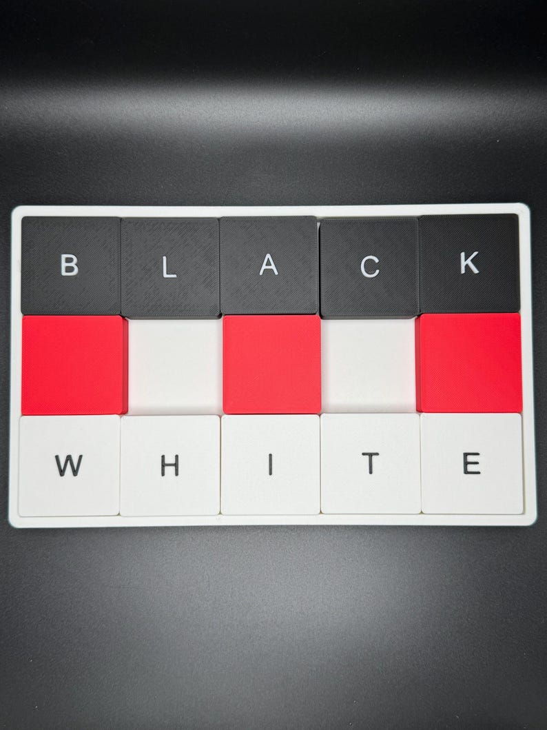 May include: A rectangular puzzle with the words "BLACK" and "WHITE" spelled out in individual letter tiles. The tiles alternate between black, red, and white, creating a visually striking contrast. The letters are in a sans-serif font.