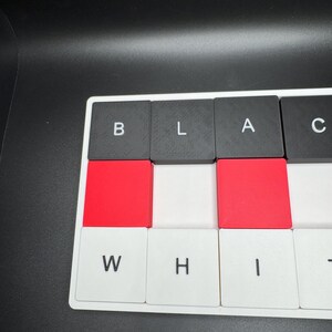 May include: Close-up of a keyboard with the letters spelling "BLACK WHITE". The keys are black, red, and white. The background is black.