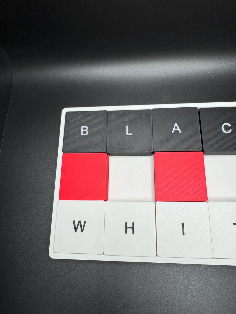 May include: Close-up of a keyboard with the letters spelling "BLACK WHITE". The keys are black, red, and white. The background is black.