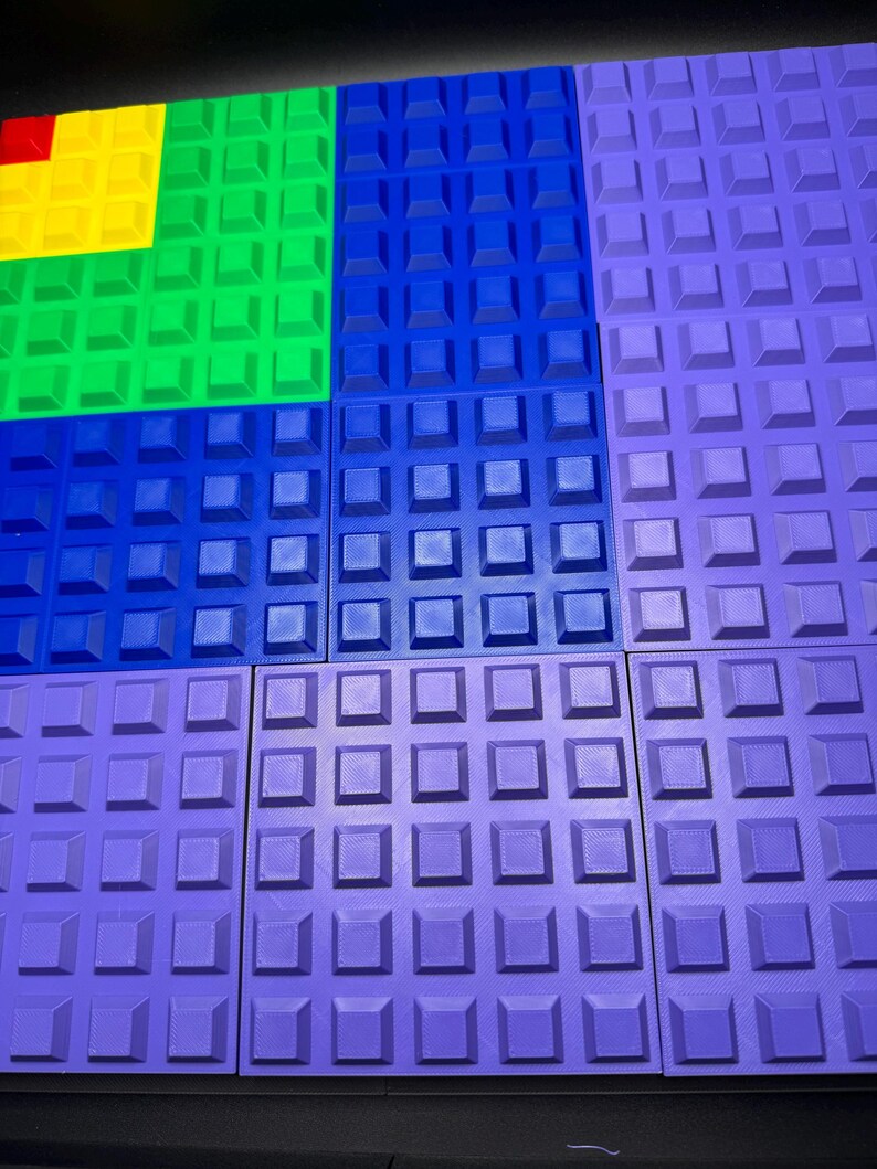 May include: A collection of colorful, textured square tiles in shades of red, yellow, green, blue, and purple. Each tile features a grid of raised square studs, creating a tactile surface. The tiles are arranged in a geometric pattern.