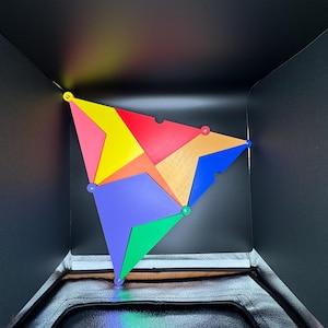 Peut inclure: Un puzzle g&eacute;om&eacute;trique color&eacute; compos&eacute; de diverses formes triangulaires et quadrilat&eacute;rales rouges, jaunes, bleues, vertes et oranges. Les pi&egrave;ces sont reli&eacute;es par de petites attaches rondes, cr&eacute;ant une structure tridimensionnelle sur fond noir.