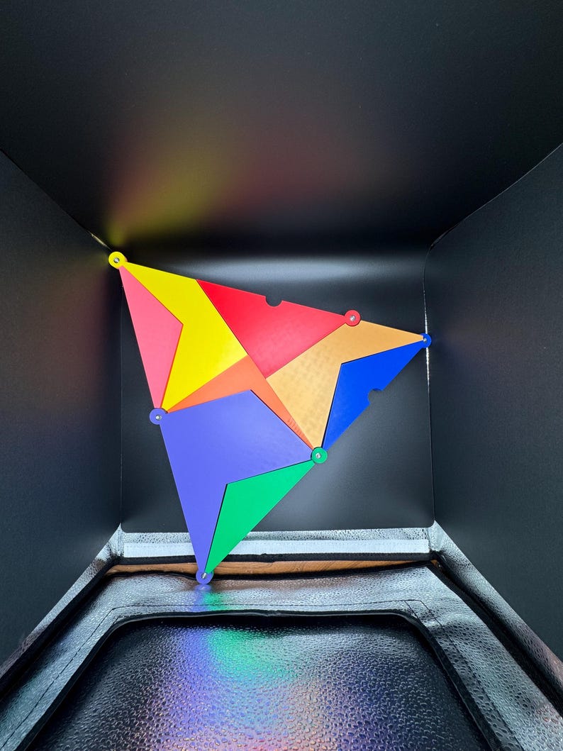 Peut inclure: Un puzzle g&eacute;om&eacute;trique color&eacute; compos&eacute; de diverses formes triangulaires et quadrilat&eacute;rales rouges, jaunes, bleues, vertes et oranges. Les pi&egrave;ces sont reli&eacute;es par de petites attaches rondes, cr&eacute;ant une structure tridimensionnelle sur fond noir.