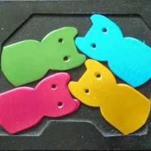 May include: A colorful puzzle featuring four cat-shaped pieces in green, blue, pink, and yellow. The pieces fit into a black, rectangular frame. Each cat-shaped piece has two circular holes.