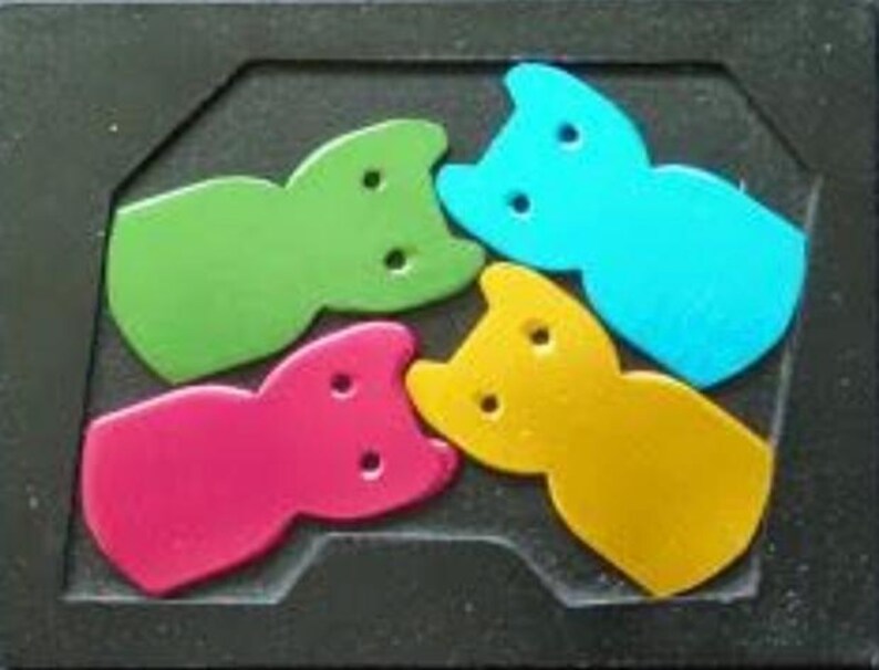 May include: A colorful puzzle featuring four cat-shaped pieces in green, blue, pink, and yellow. The pieces fit into a black, rectangular frame. Each cat-shaped piece has two circular holes.
