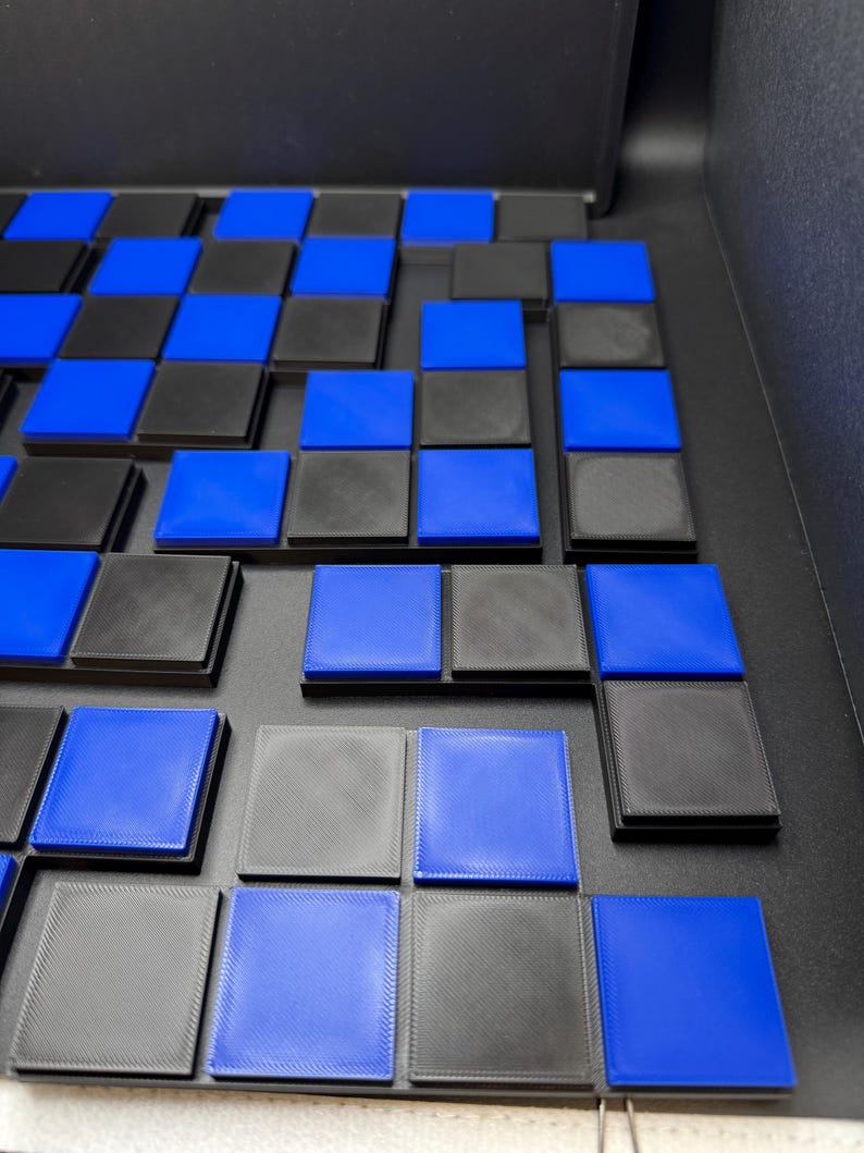 May include: A partially assembled board game with a checkerboard pattern. The squares alternate between black and blue. The game pieces are square and have a raised edge. The board is black.
