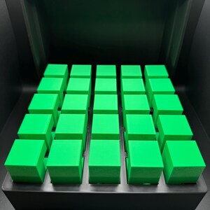 May include: A black box with a lid open, revealing a grid of 36 bright green cubes.