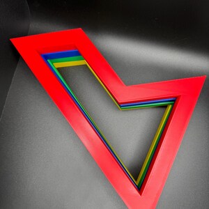 May include: A set of five nested geometric shapes, each with a different color. The shapes are red, blue, green, yellow, and a lighter shade of green. The shapes are arranged in a V-shape.