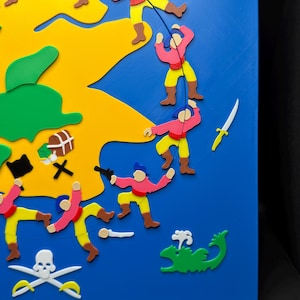 May include: A colorful, 3D-printed pirate-themed artwork. The piece features a blue background with a yellow island, green sea monster, and various pirate figures in pink, yellow, and brown. Includes a skull and crossbones, crossed swords, and a treasure chest.