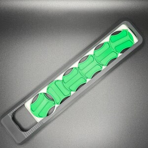 May include: A black and white plastic tool with six green circular compartments. The tool has a handle with a hole in it.