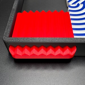 May include: A red plastic tray with a zig-zag edge and a red plastic handle. The tray is empty.