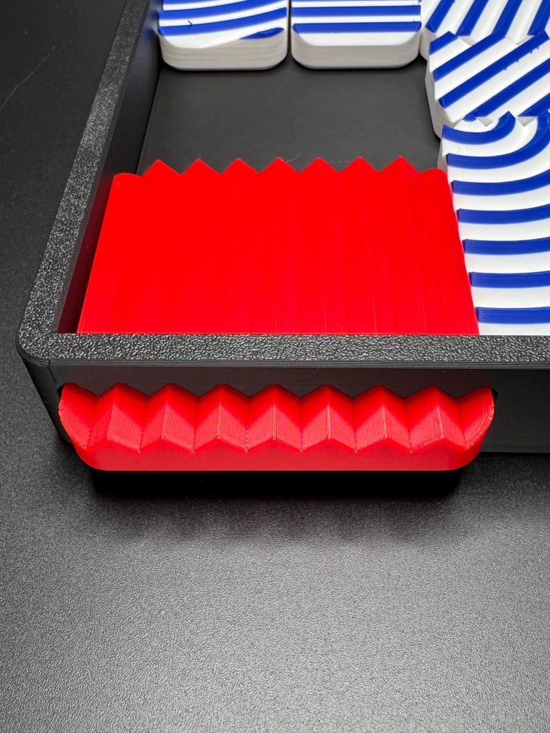 May include: A red plastic tray with a zig-zag edge and a red plastic handle. The tray is empty.