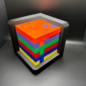 May include: A colorful block puzzle with a variety of shapes and colors. The puzzle is assembled in a square frame and is made of plastic.