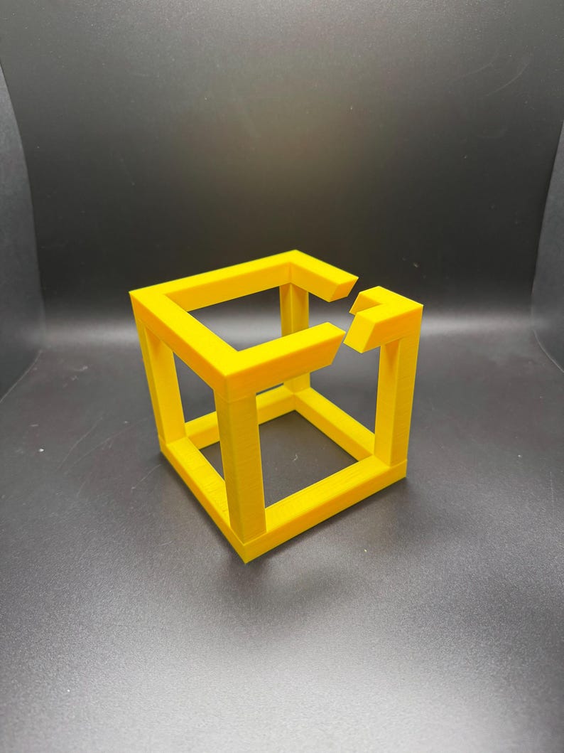 May include: A bright yellow impossible cube sculpture, a 3D printed optical illusion. The cube appears to defy the laws of physics with its interconnected, yet disjointed, structure. The object is set against a dark background.