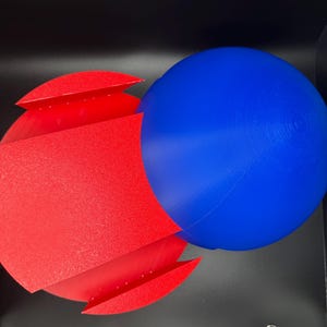 Puede incluir: Un conjunto de formas geom&eacute;tricas rojas y azules. La forma roja es una forma tridimensional, doblada y curvada. La forma azul es una esfera.