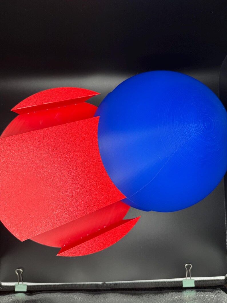 Puede incluir: Un conjunto de formas geom&eacute;tricas rojas y azules. La forma roja es una forma tridimensional, doblada y curvada. La forma azul es una esfera.