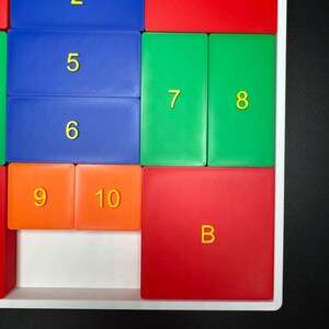 K&ouml;nnte beinhalten: Ein farbenfrohes Puzzlespiel mit nummerierten Kacheln in Orange, Blau und Gr&uuml;n. Die Kacheln sind in einem Raster angeordnet, wobei die Buchstaben 'B' und 'C' auf den roten Kacheln stehen.